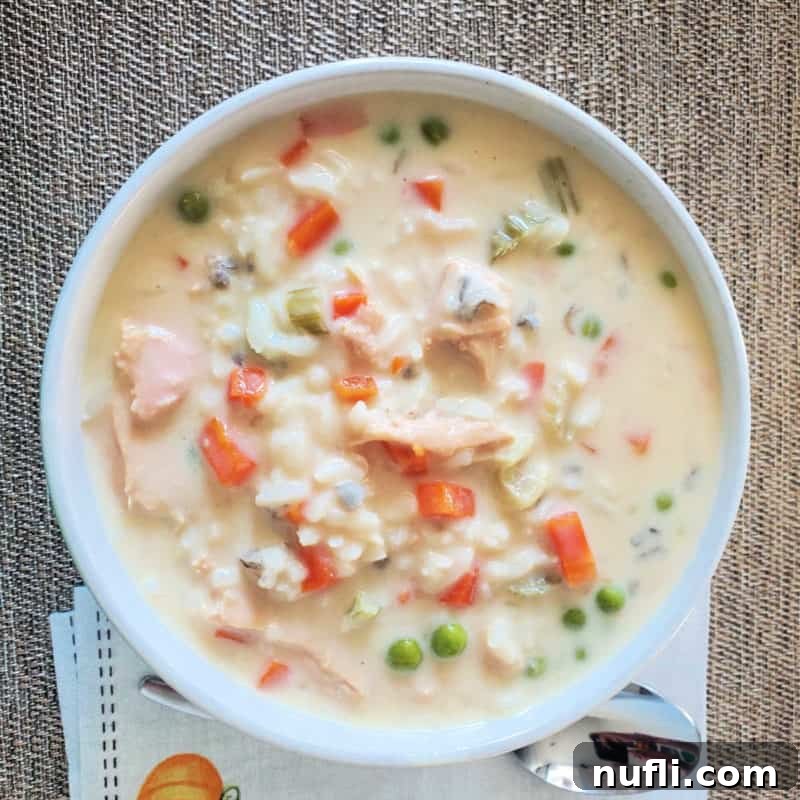 Turkey wild rice soup in a white bowl next to a silver spoon and napkin