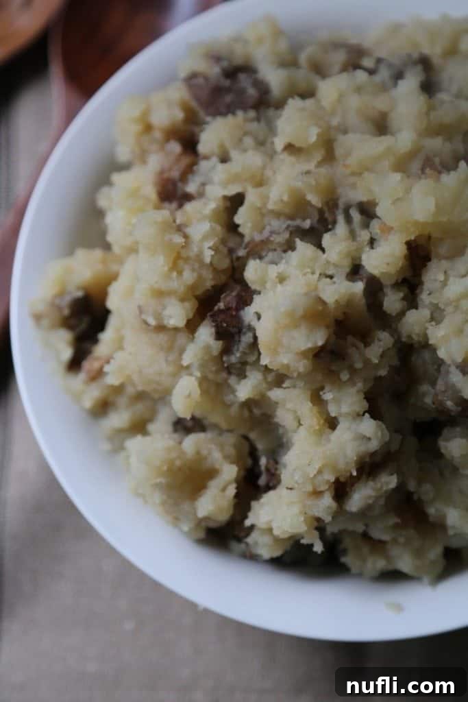 A close-up of creamy Crock Pot Garlic Mashed Potatoes in a white bowl, garnished with fresh herbs, sitting on a rustic brown placemat.