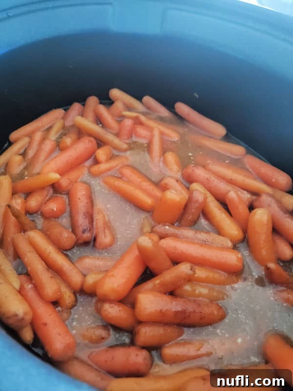 Close-up of crock pot carrots cooking in a black slow cooker, showcasing the simmering glaze.