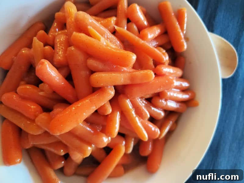 Glazed Carrots in a white serving bowl with a wooden spoon, perfect for a holiday meal.