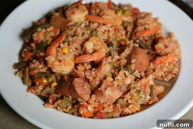 Close-up of a serving of Crock Pot Kielbasa and Shrimp Stew in a white bowl, showing the rich broth, pieces of kielbasa, shrimp, okra, and mixed vegetables.