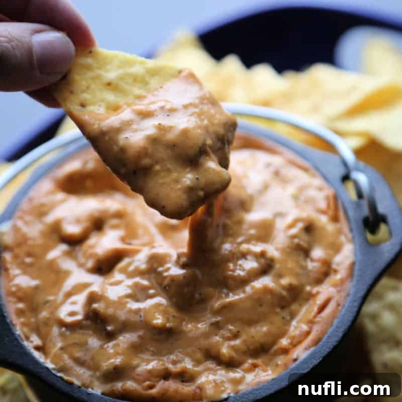 Easy Slow Cooker Appetizers 13 Hand holding a chip dipping into a bowl of Chili's Queso