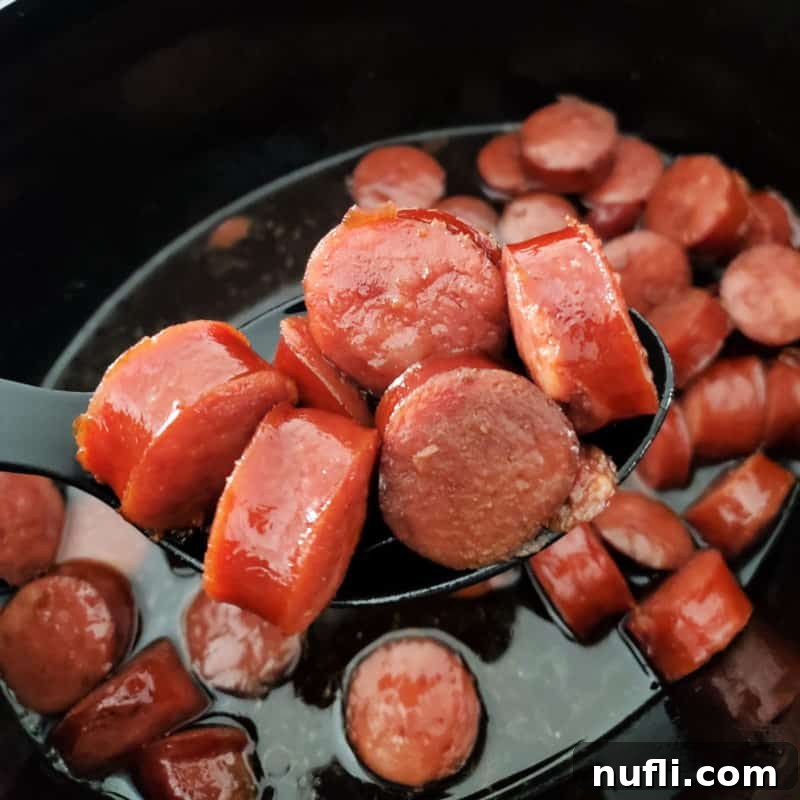 Easy Slow Cooker Appetizers 14 A slow cooker bowl with a spoon lifting cut kielbasa, coated in a sweet glaze