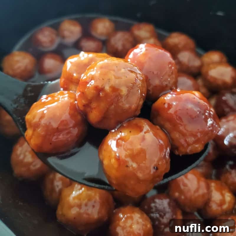 Easy Slow Cooker Appetizers 24 Grape Jelly Meatballs on a plastic serving spoon above a slow cooker