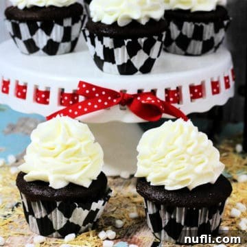 Close-up of a single Hot Chocolate Cupcake with marshmallow frosting and cocoa powder, in a decorative paper liner.