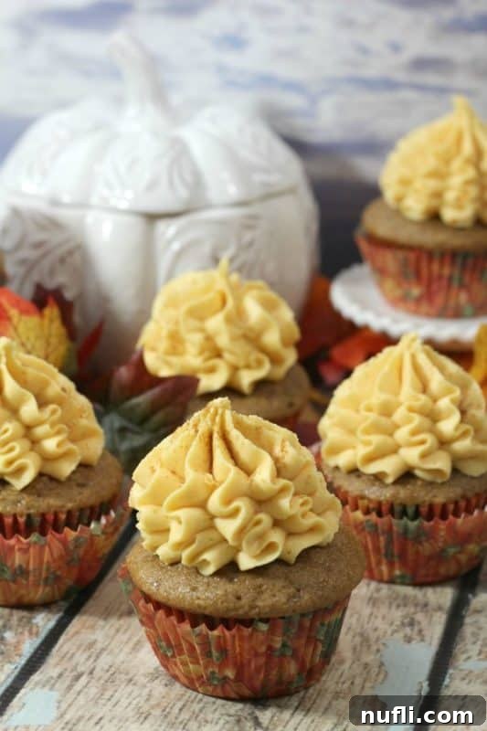 Spiced Pumpkin Cupcakes with Maple Frosting 2 Maple-frosted pumpkin cupcakes next to a decorative white pumpkin, beautifully arranged for a fall dessert spread