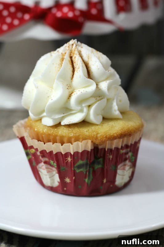 Festive eggnog cupcake with smooth white frosting in a vibrant Santa red cupcake liner, topped with a sprinkle of cinnamon, ready for holiday celebrations
