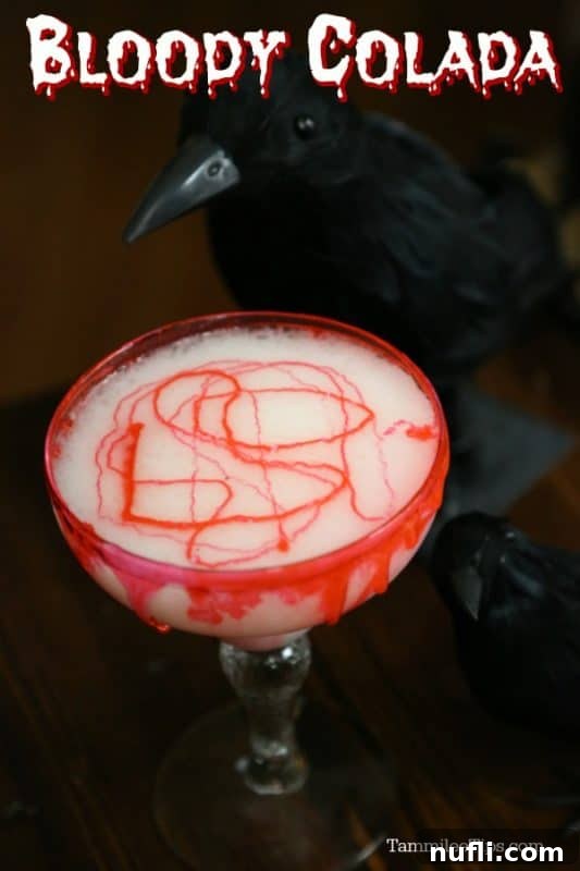 Bloody Colada over a margarita glass with fake blood on the side of it next to a crow