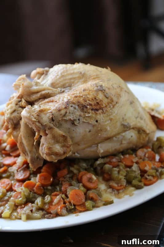 Cooked Crockpot turkey on a white serving platter with carrots, celery, and onions, garnished with fresh herbs.