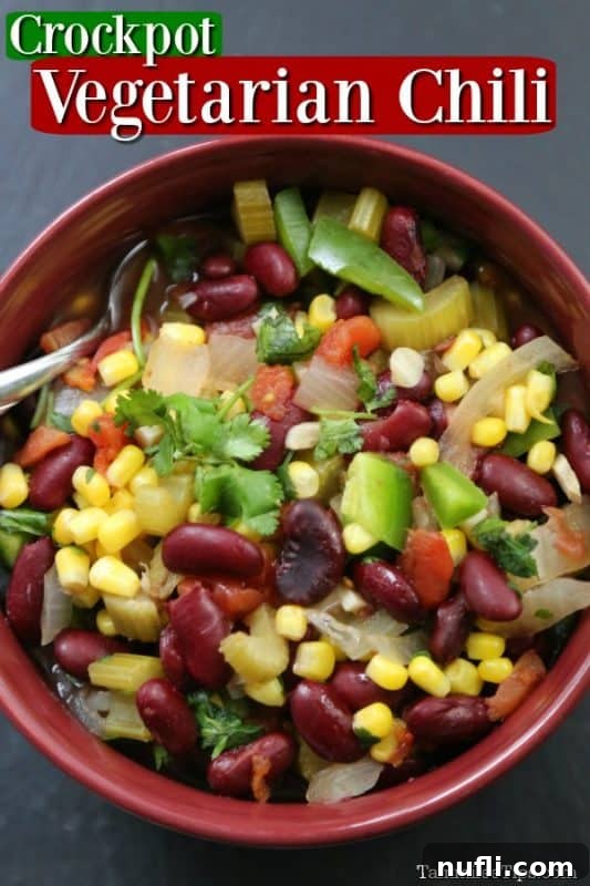 A vibrant bowl of Crockpot Vegetarian Chili, featuring corn, beans, celery, and peppers, rests on a rustic gray background with a silver spoon poised within.