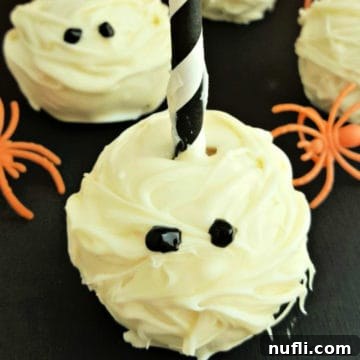 Close-up of a finished Mummy Cake Pop next to a few orange plastic spiders, highlighting its festive look.