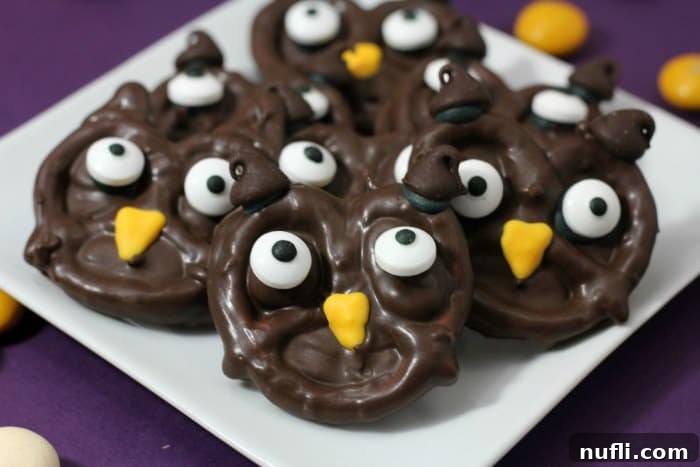 Close-up of three charming owl pretzels, each with chocolate ears, candy eyes, and a bright yellow icing beak, stacked on a white plate.