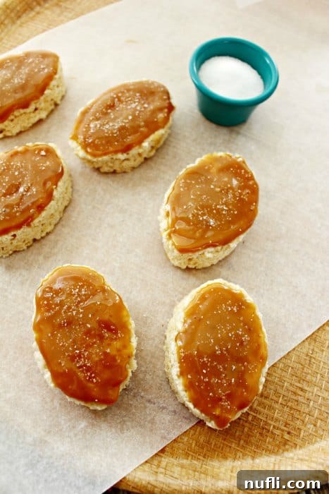 Rice Krispie ovals with salt on them sitting on parchment paper, ready for caramel sauce application.