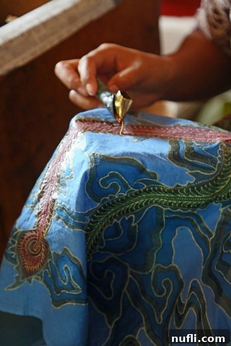Artisan's hands meticulously applying wax to create intricate patterns on a vibrant batik fabric, highlighting the skill and detail involved