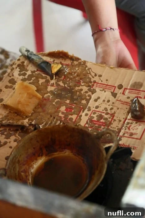 Close-up of wax-covered patterns on a fabric piece, alongside various batik tools, illustrating the resist dyeing technique