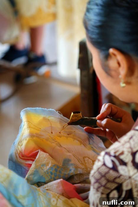 Balinese woman meticulously working on a large piece of batik fabric, demonstrating intricate hand-drawn wax designs
