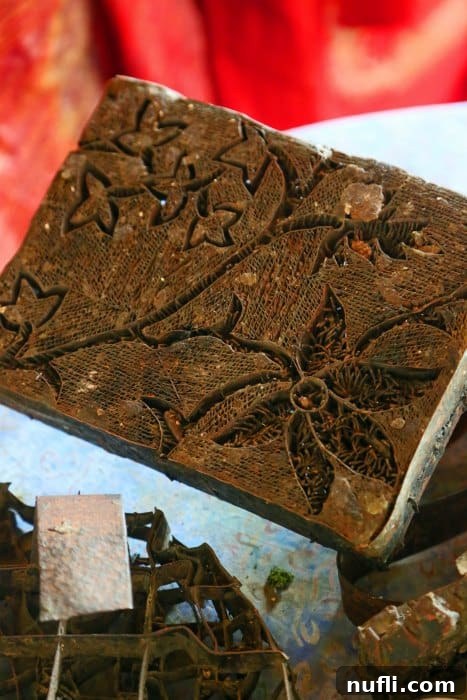 Detailed flower pattern being applied onto fabric using a traditional wooden batik stamp (cap)