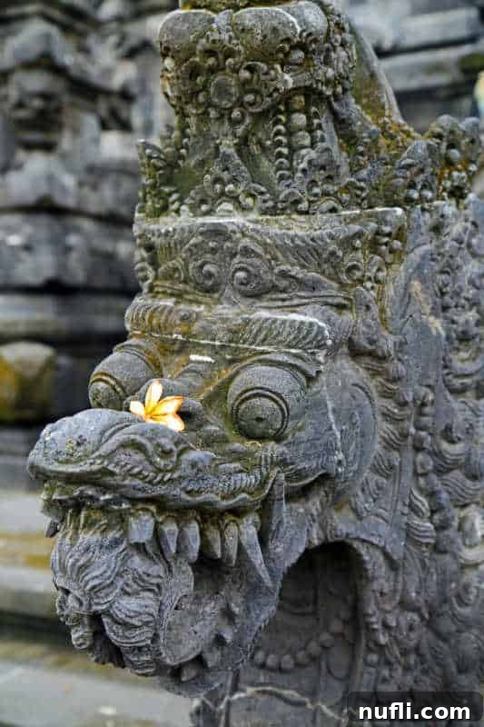 Close-up of a intricately carved stone statue at a Balinese temple, adorned with a fresh frangipani flower as an offering.