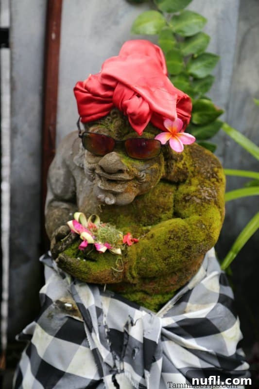 Bali's Tirta Gangga: Royal Water Gardens 3 Close-up of a Balinese guardian statue adorned with sunglasses, a vibrant red scarf, and fresh flowers, showcasing cultural charm.