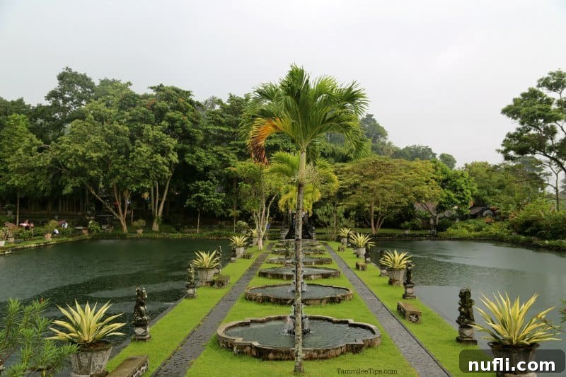 Bali's Tirta Gangga: Royal Water Gardens 7 The central water palace area featuring elegant palm trees symmetrically lining the middle of a grand pond, flanked by ancient statues.