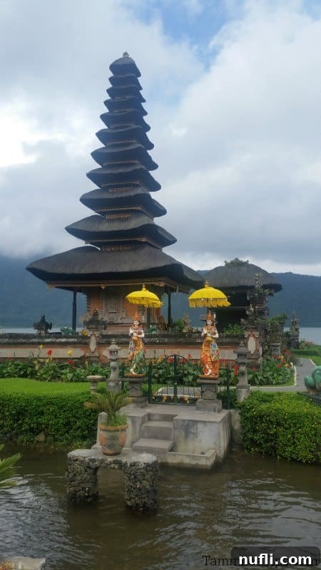 Two intricate guardian statues stand before the multi-tiered pagoda of Ulun Danu Beratan Temple, on a slightly cloudy day