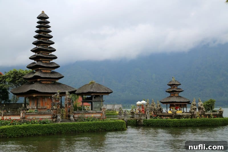 Panoramic view of multiple Ulun Danu Beratan Temple structures gracefully rising from Lake Bratan's surface on a cloudy, atmospheric day