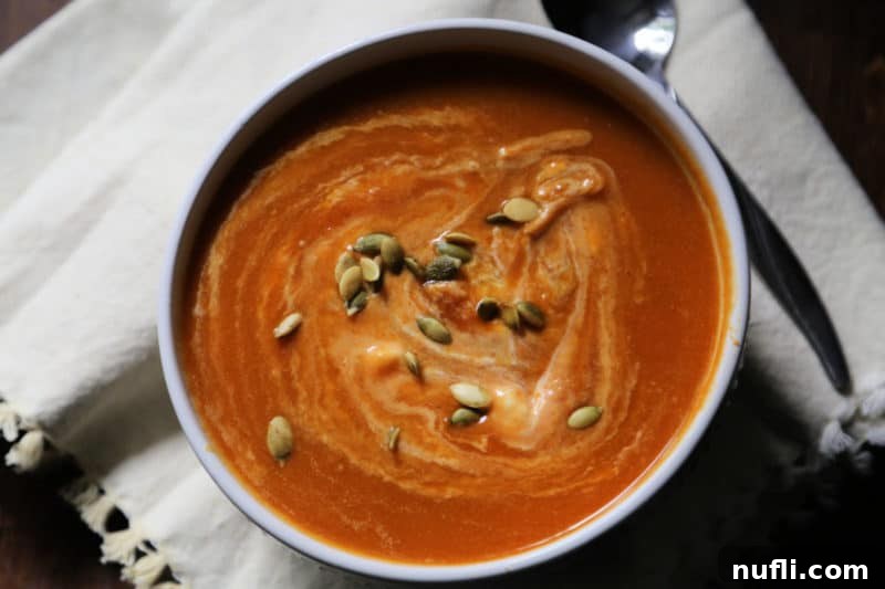 pumpkin soup topped with seeds in a white bowl next to a spoon