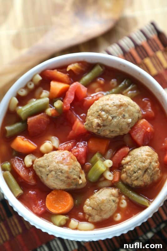 Close-up of a white bowl filled with Crockpot Vegetarian Meatball Soup, showing the rich texture and vegetables.