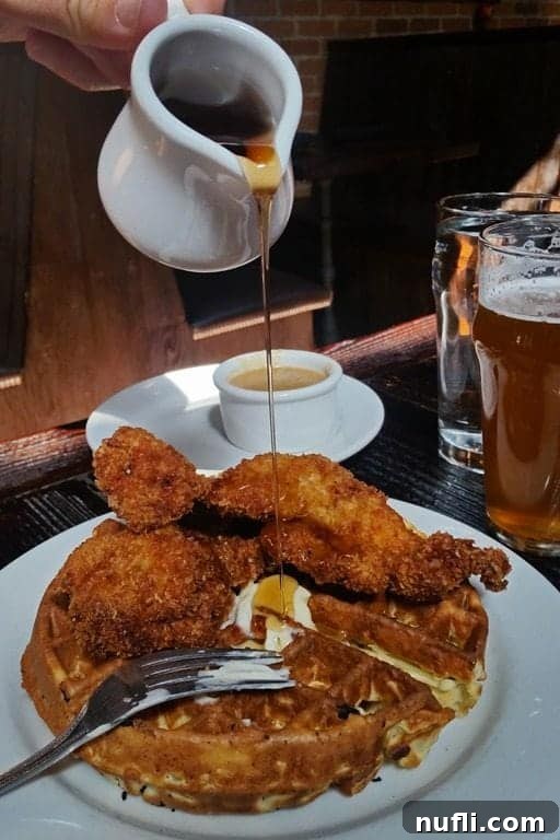 Chicken and waffles dish with golden syrup being poured over crispy chicken, on a white plate