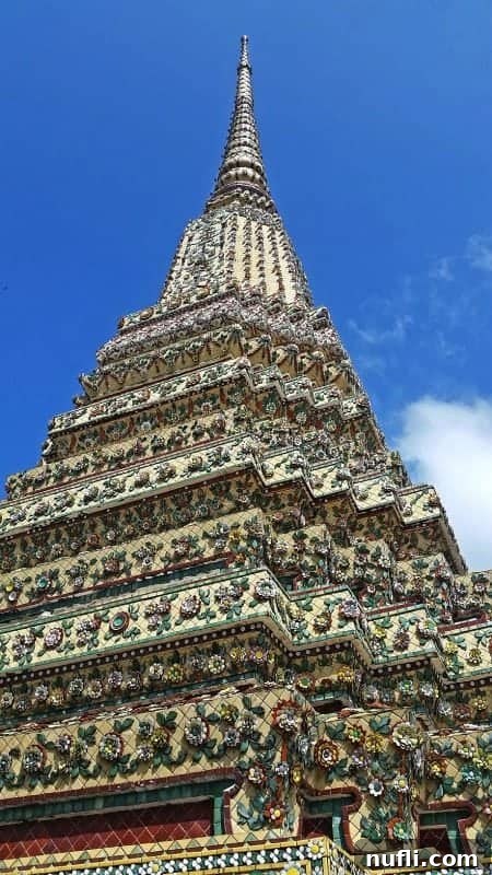 Intricate roof and spire detail of a temple building at Wat Pho, Bangkok, highlighting its multi-tiered golden and colorful architecture.