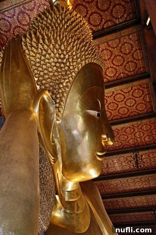 Close-up view of the serene and gilded face of the Reclining Buddha at Wat Pho, highlighting its intricate features.