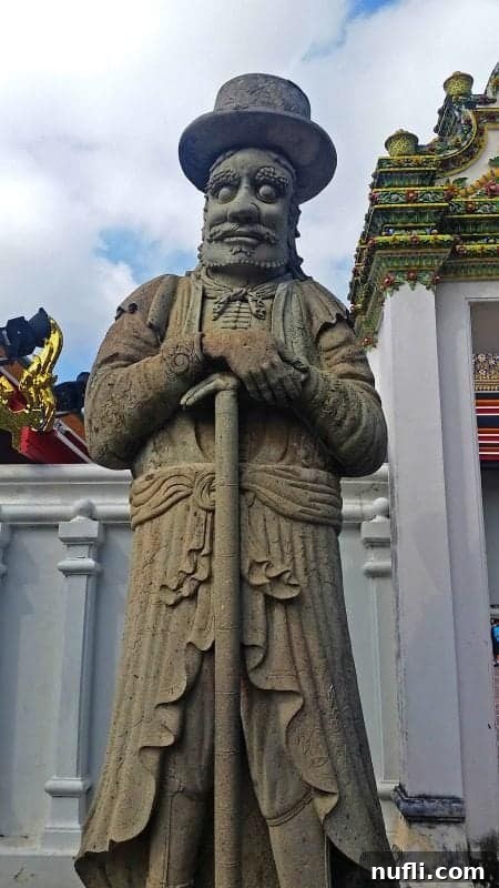 Detailed stone guardian figurine with a long coat and staff, representing the protective figures at Wat Pho temple entrances.