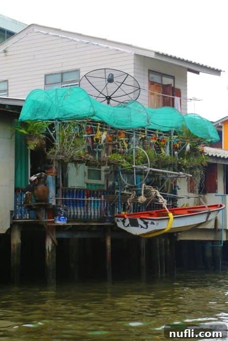 Bangkok Chao Phraya River Cruise 7 A traditional house built on stilts along the Chao Phraya River, featuring a small boat tied to its deck, illustrating riverine living.