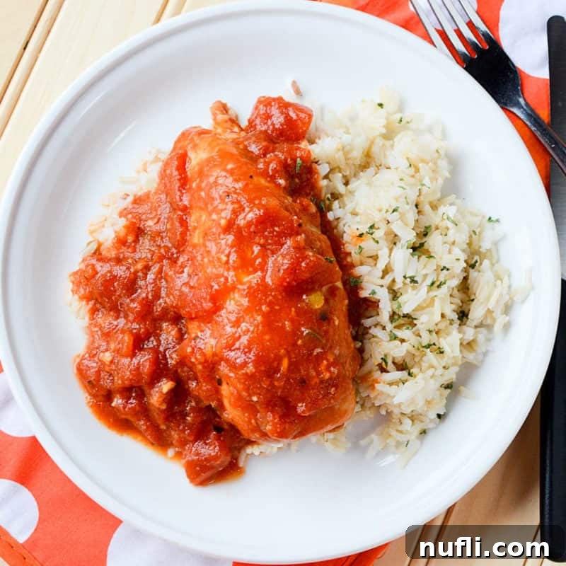 Vibrant Tex-Mex chicken served alongside white rice on a white plate, with a fork at the ready for a delightful meal.