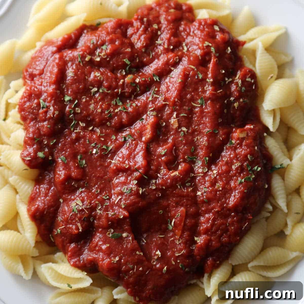 Over 40 Simple Plant-Based Slow Cooker Meals 21 a white plate with marinara sauce on pasta shells, a simple and flavorful Italian sauce