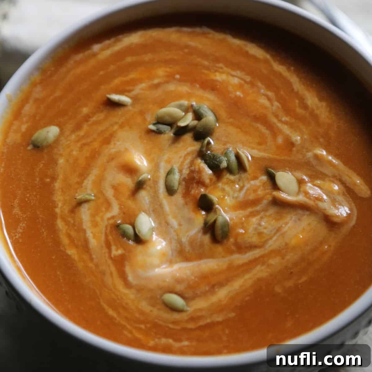 Over 40 Simple Plant-Based Slow Cooker Meals 34 Crockpot Pumpkin Soup garnished with pepita seeds in a white bowl, a creamy and flavorful autumn soup