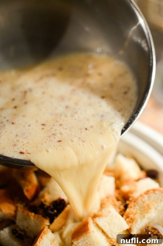 Eggnog batter being poured over cubed bread and cranberries in a slow cooker bowl, ready for cooking.