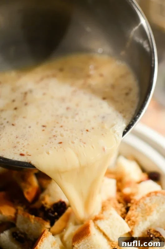 Eggnog batter being poured over cubed bread and cranberries in a slow cooker bowl, ready for cooking.