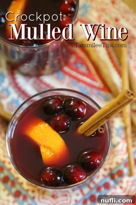 Crockpot mulled wine served in two glasses, garnished with red wine, fresh cranberries, orange peel, and cinnamon sticks.