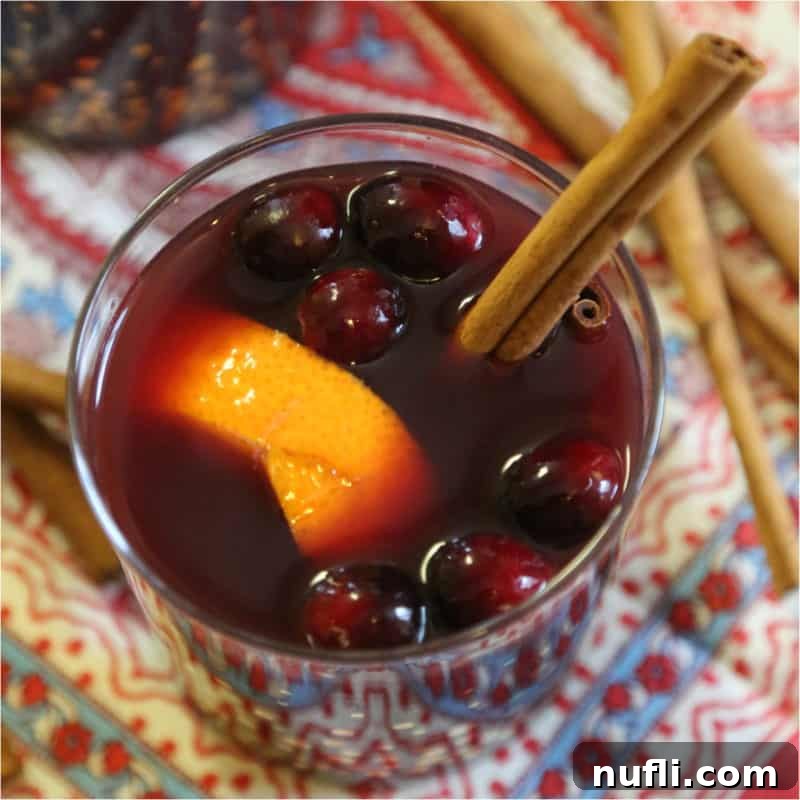 Warm mulled wine in a glass mug, garnished with an orange slice, fresh cranberries, and a cinnamon stick.