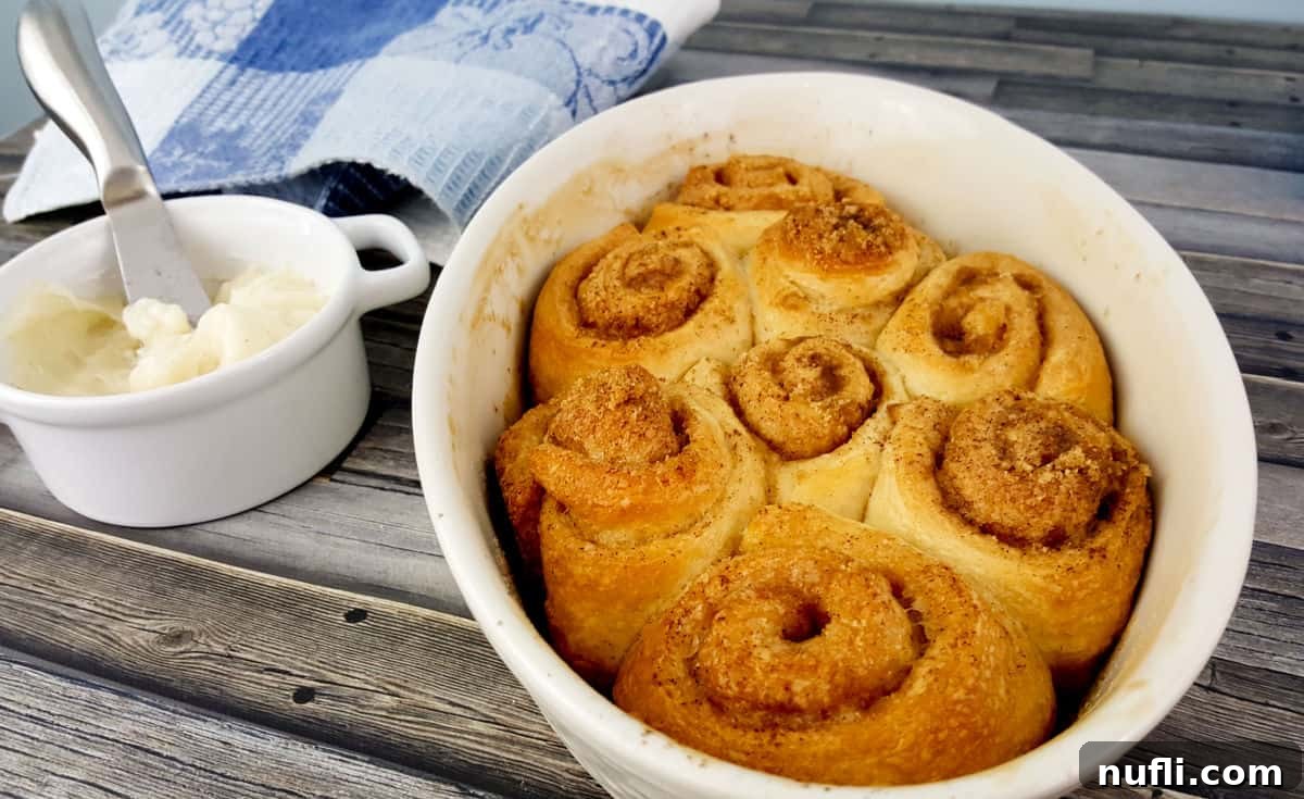 baked cinnamon rolls in a white dish next to a container of frosting. Perfect for breakfast or brunch.
