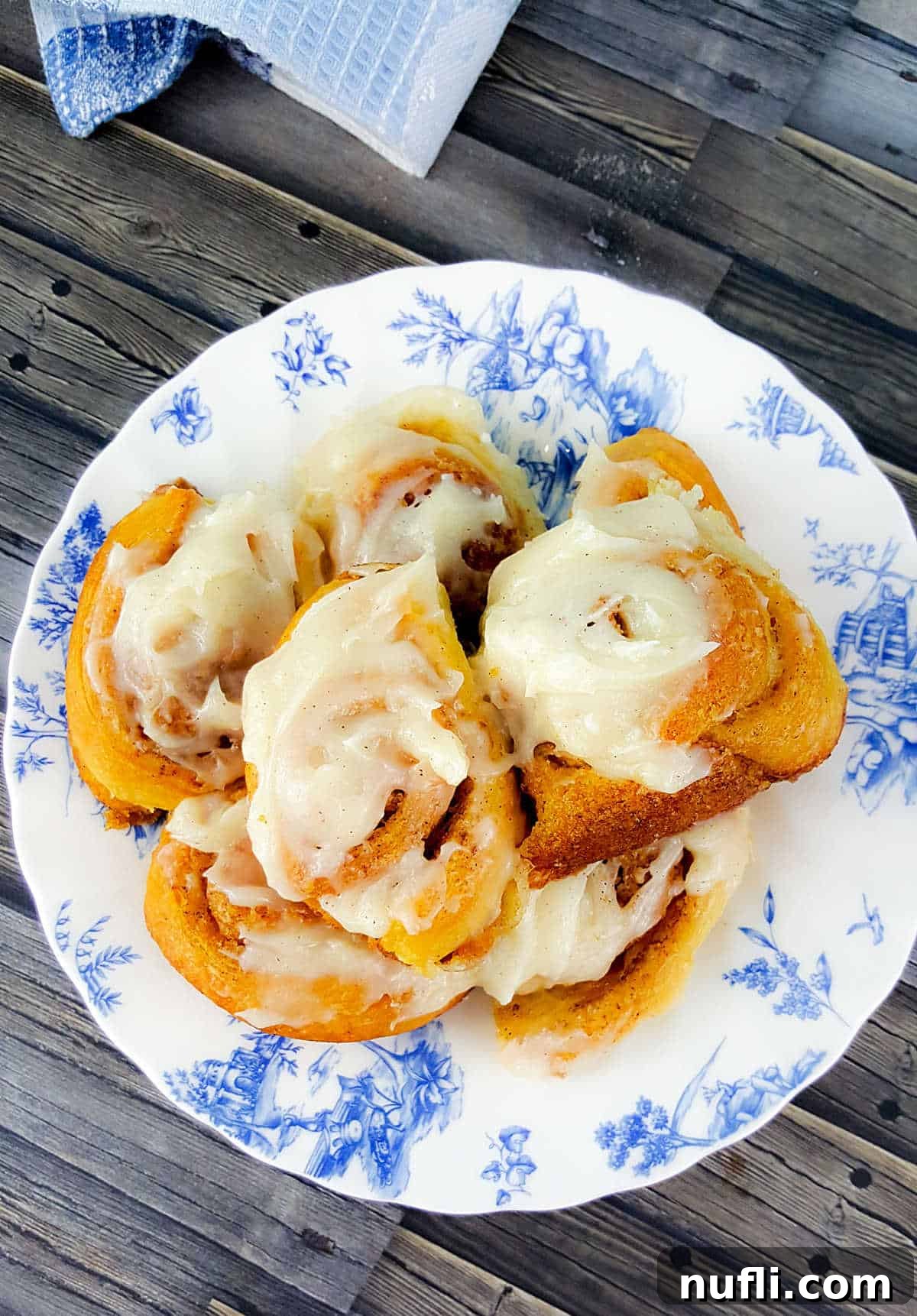 iced cinnamon rolls on a blue and white plate, ready to be enjoyed.