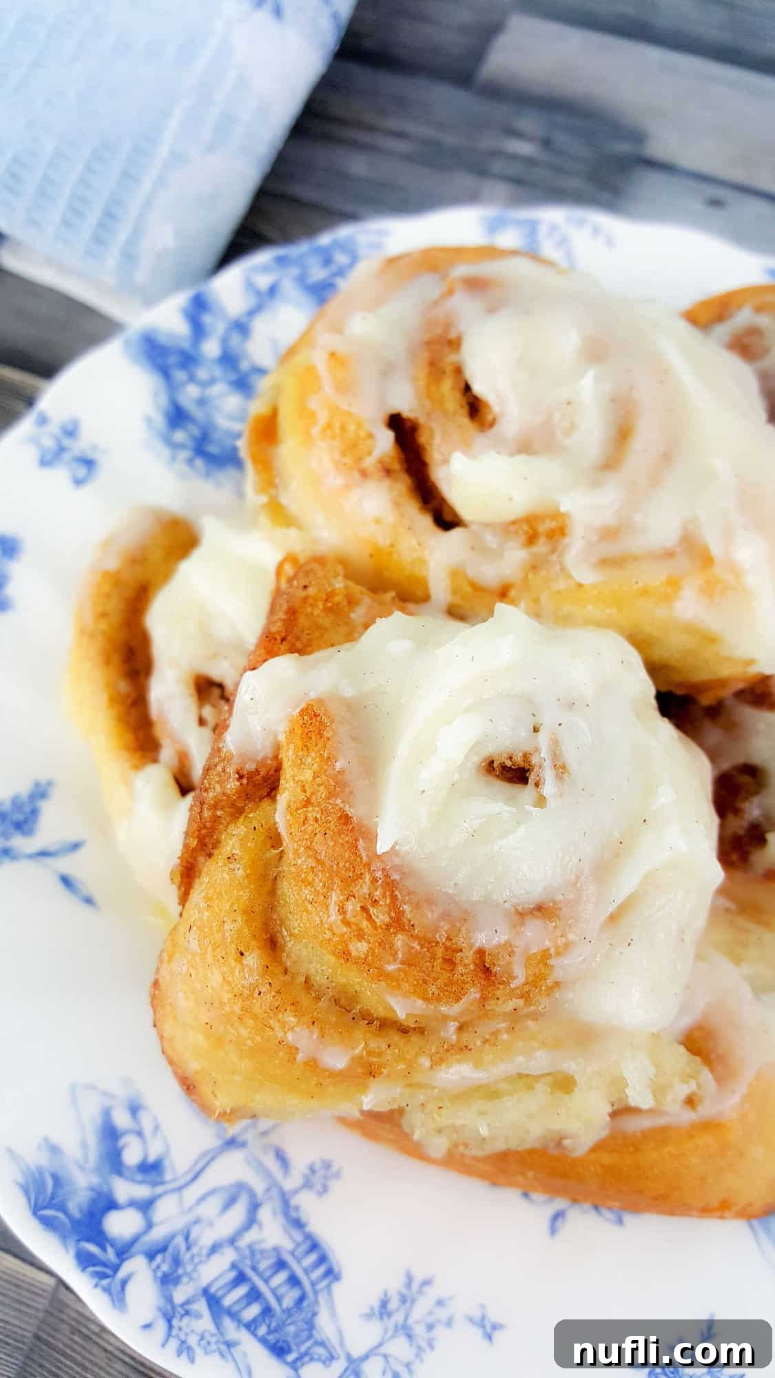 close up of iced cinnamon rolls on a white and blue plate, showcasing the delicious frosting and swirl.