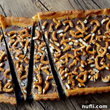Sweet and Salty Chocolate Dessert Bar topped with pretzel on a wood board, showcasing its rich layers and crunchy topping.