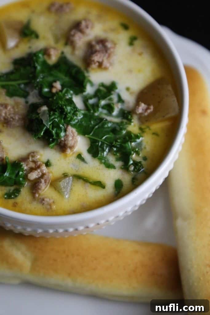 A close-up shot of the Crock Pot Copy Cat Olive Garden Zuppa Toscana Soup Recipe, showing a rich and creamy broth with visible chunks of sausage, potatoes, and kale.