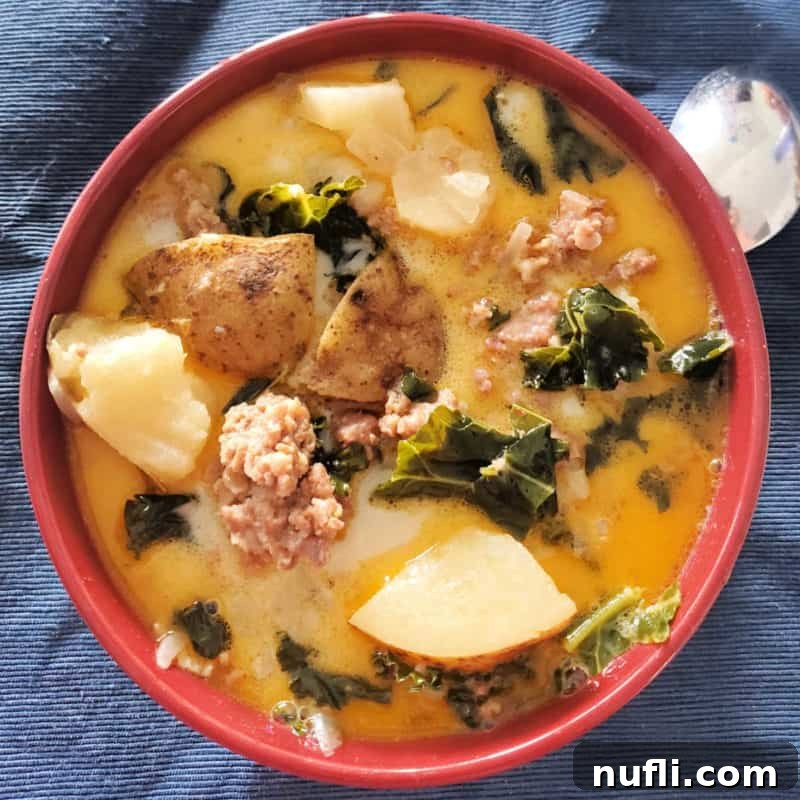 A vibrant red bowl filled with Olive Garden Zuppa Toscana Soup, showcasing the rich broth, tender ground beef, diced potatoes, and fresh kale.