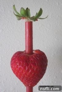 Strawberry Hulling - Stem Removal The straw pushing through the top of a strawberry, removing the stem and core.