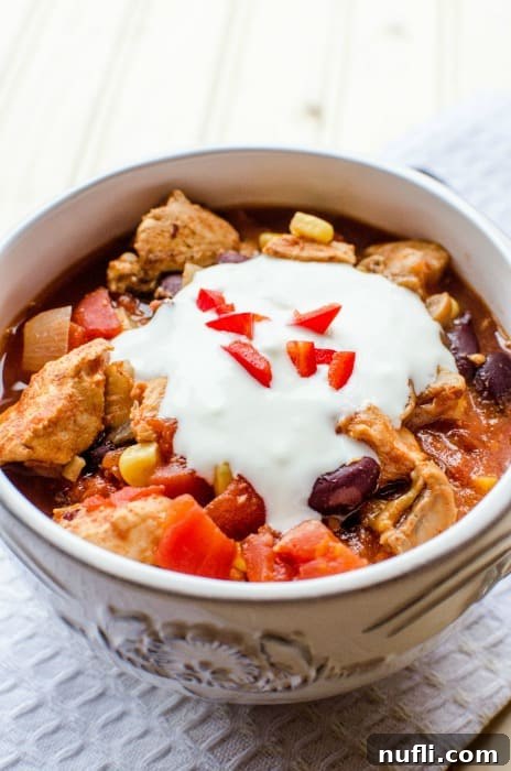 Zesty Slow Cooker Southwest Chicken Chili 3 bowl of chili topped with sour cream, next to a silver spoon on a white napkin
