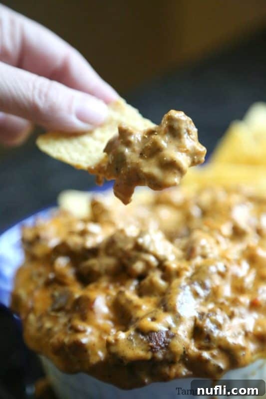 Ultimate Meat Lovers Crock Pot Queso Dip 3 A hand holding a tortilla chip above a bowl of rich, bubbling Meat Lovers Slow Cooker Queso Dip.
