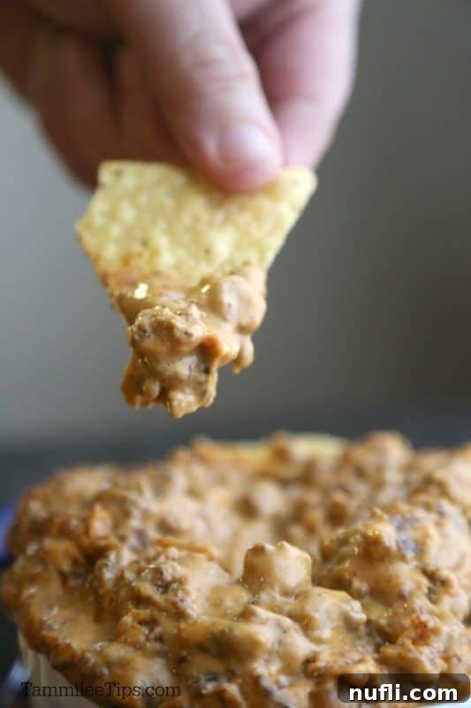 Hearty Meat Lover's Crockpot Queso Dip 4 A close-up shot of a hand dipping a tortilla chip into a delicious bowl of Meat Lovers Queso.